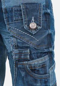 Pantaloni cargo in denim blu scuro, dotati di molteplici tasche, cuciture arancioni a contrasto e un dettaglio di bottone metallico sul davanti.