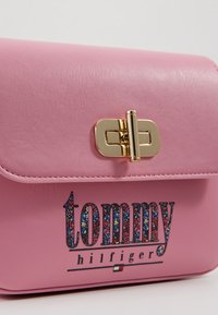Rosa læderhåndtaske med en guld hardwarelås. Udstyret med blomstertekstlogoet "tommy hilfiger" i multifarvede designs. Glat tekstur.