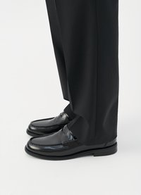 Μαύρο δερμάτινο loafers με λεία υφή και διακοσμητική ραφή, συνδυασμένα με κομμένα μαύρα παντελόνια, από την ακριβώς πάνω από τον αστράγαλο και κάτω.