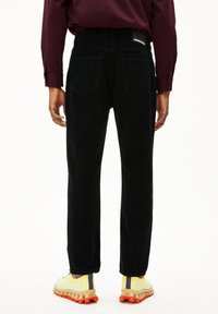 Zwarte corduroy broek met twee achterzakken, rechte pasvorm en een gestructureerd oppervlak. Gepaarde met gele en grijze sport schoenen.