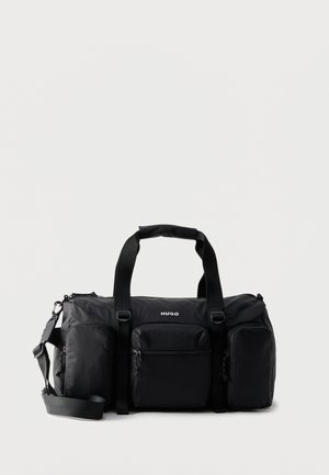 Čierna taška Hugo typu duffel s tromi prednými vreckami na zips, dvoma hornými rukoväťami a nastaviteľným ramenným popruhom na bielom pozadí.