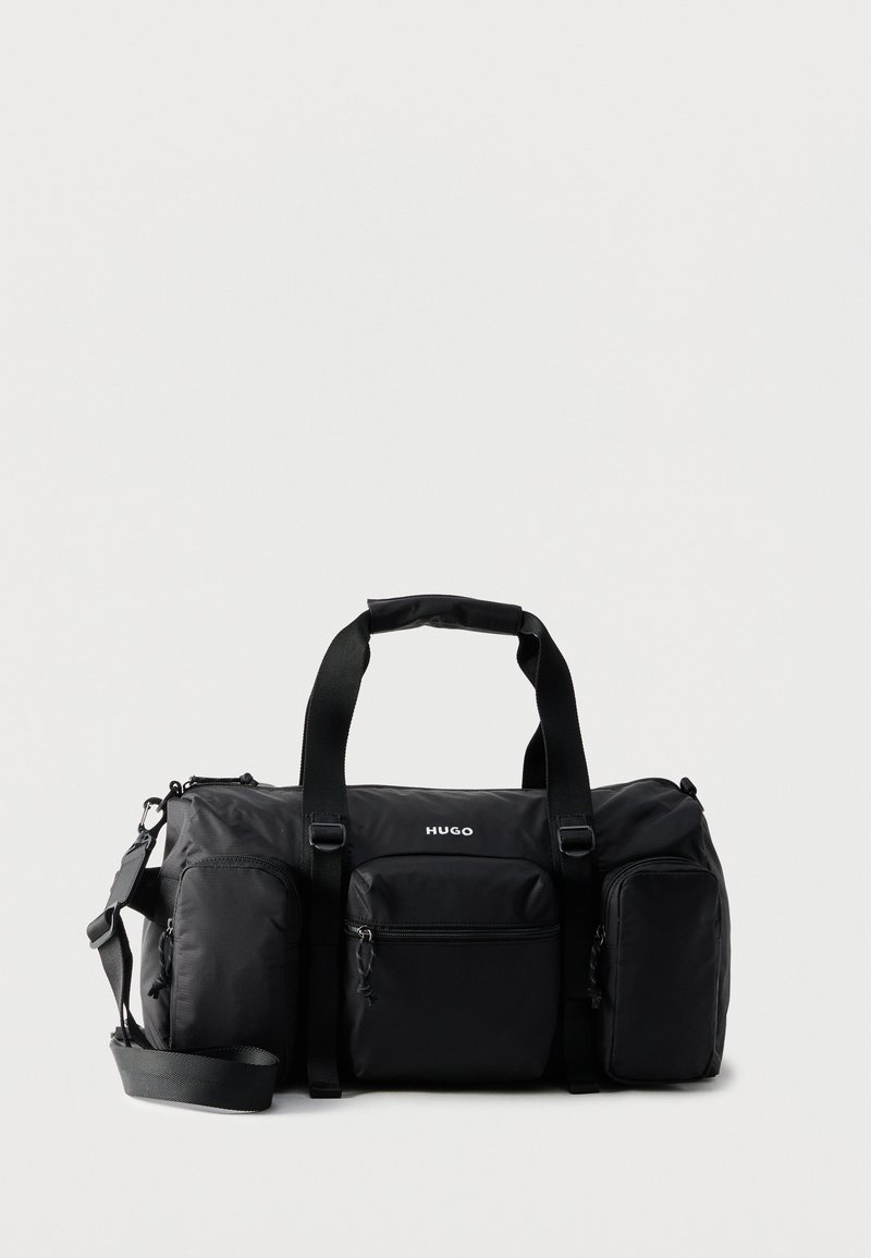 Μαύρη τσάντα τύπου Hugo duffel με τρεις μπροστινές τσέπες με φερμουάρ, δύο επάνω χερούλια και ρυθμιζόμενο λουρί ώμου σε λευκό φόντο.