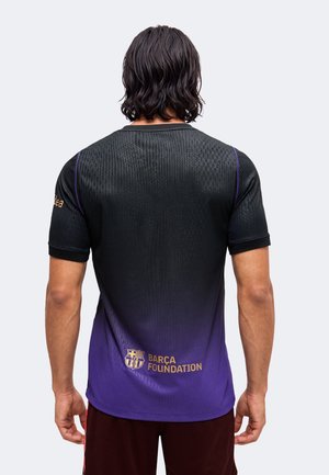 Persona con cabello oscuro que lleva una camiseta deportiva negra y morada con el texto y el logo "BARÇA FOUNDATION" en la parte baja de la espalda.