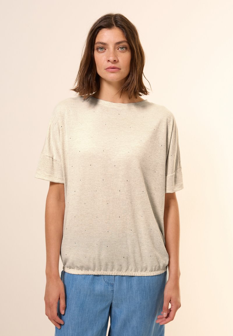 T-shirt grigio chiaro a maniche corte con una vestibilità ampia, caratterizzato da piccole macchie blu, colletto rotondo e orlo elastico sul fondo. Abbinato a pantaloni blu.