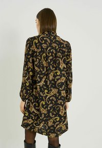 Vestido negro con un estampado de cachemira en dorado y marrón. Mangas largas, escote fruncido, longitud media y silueta relajada. Tejido liso.