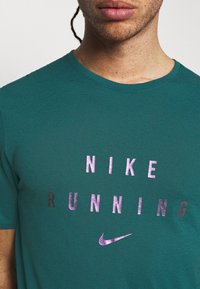 Teal Nike Running t-shirt features the brand name and logo in glossy black and purple print, with a smooth, textured fabric.
