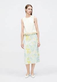 Haut sans manches crème orné d'une bordure en tissu fleur, assorti à une jupe longue brodée de fleurs bleues et jaunes.