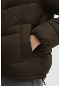 Braune Pufferjacke mit gestepptem Design und Seitentaschen. Sie zeichnet sich durch eine glatte Textur und elastische Bündchen aus, mit einem Logotag am unteren Saum.