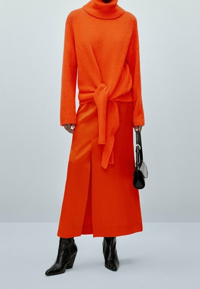 Orange knitted turtleneck sweater with a tied waist, paired with a matching orange midi skirt featuring a front slit, and black ankle boots.