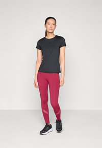 Black short-sleeve athletic top, paired with fitted burgundy leggings featuring mesh accents and textured surfaces. Black athletic shoes complete the look.