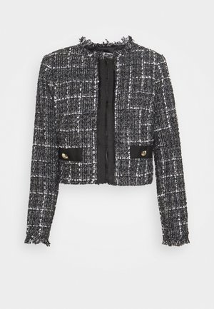 Chaqueta corta de tweed en blanco y negro con bordes deshilachados, mangas largas, dos bolsillos frontales con botones dorados y cuello redondo.