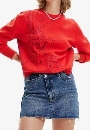 Kvinde iført en rød sweater med Bugs Bunny-grafik og en blå denim mininederdel, accessoriseret med en kort sølvhalskæde.