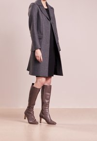 Szary płaszcz z mieszanki wełny z klapami, z przodu guziki i bocznymi kieszeniami; w komplecie z brązowymi skórzanymi kozakami do kolan i czarną sukienką.