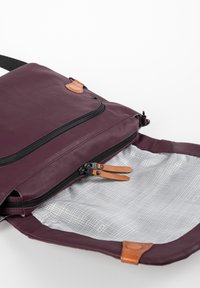 Borsa a spalla viola con tirazip in pelle, aperta per mostrare l'interno grigio chiaro foderato con un motivo a griglia e chiusura a calamita.