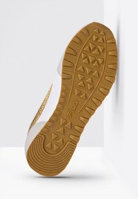 Semelle de basket blanche avec accents dorés, caoutchouc texturé pour une meilleure adhérence, présentant un motif de bande de roulement avec des formes triangulaires et angulaires.