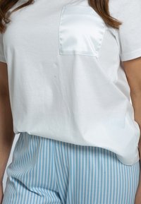 T-shirt bianco in cotone con tasca in raso, abbinato a pantaloni a vita alta a righe bianche e blu chiaro. Texture liscia in tutto.