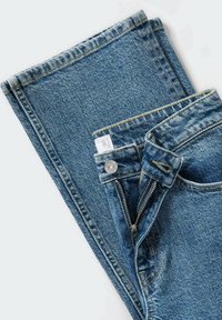 Jeans de mezclilla azul claro con cremallera y cierre de botón. Presentan costuras amarillas y un dobladillo en la cintura.