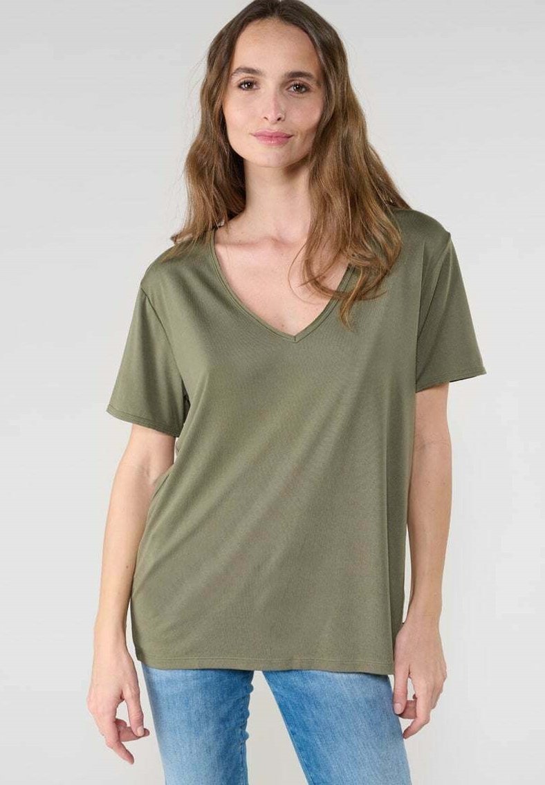 Camiseta verde oliva de manga corta y escote en V, hecha de un tejido suave y liso con un corte relajado, combinada con unos vaqueros azul claro.