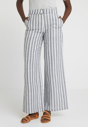 Breda byxor med blå och vita vertikala ränder, som har ett bälte vid midjan, sidofickor och lätt material. Bruna sandaler med remmar.