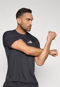 Camiseta deportiva negra hecha de material ligero, con un logotipo gris de Adidas en el pecho, de ajuste holgado y mangas cortas.