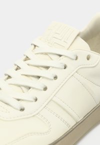 Άσπρο δερμάτινο παπούτσι σνίκερ με υφασμένα στοιχεία, στρογγυλά κορδόνια και διακριτικό λογότυπο στη γλώσσα. Διαθέτει ραμμένες λεπτομέρειες και λαστιχένια σόλα.