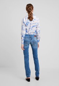 Světlomodré tričko s dlouhým rukávem a tie-dye vzorem, zkombinované s slim-fit džíny středně modré barvy. Džíny mají zadní kapsy s jemnými detailem šití.