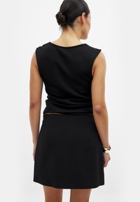 Top senza maniche nero con scollo rotondo e silhouette aderente, abbinato a una gonna a trapezio coordinata. Tessuto liscio, design minimale.