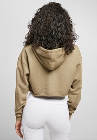 Īss kapuces džemperis no bēša kokvilnas materiāla ar kapuci. Tam ir garas piedurknes un smalks tekstūras raksts, kā arī taisna apakšējā mala.