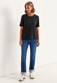 Sort kortærmet t-shirt med rund udskæring, parret med højtaljede blå jeans med opbrettede ærmer og hvide sneakers med grå detaljer.