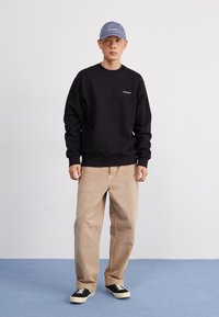 Black sweatshirt with ribbed cuffs, beige loose-fitting pants, and black sneakers. Accessories include a light blue cap. Simple, casual attire.