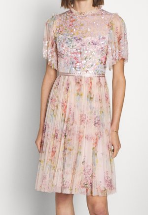 Frau trägt ein knielanges, hellrosa Blumen-Kleid mit kurzen, transparenten Ärmeln und Paillettenverzierungen am oberen Teil des Oberkörpers.