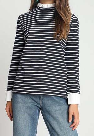 Person wearing a navy and white horizontal striped long-sleeve top with white ruffle collar and cuffs, paired with blue jeans.