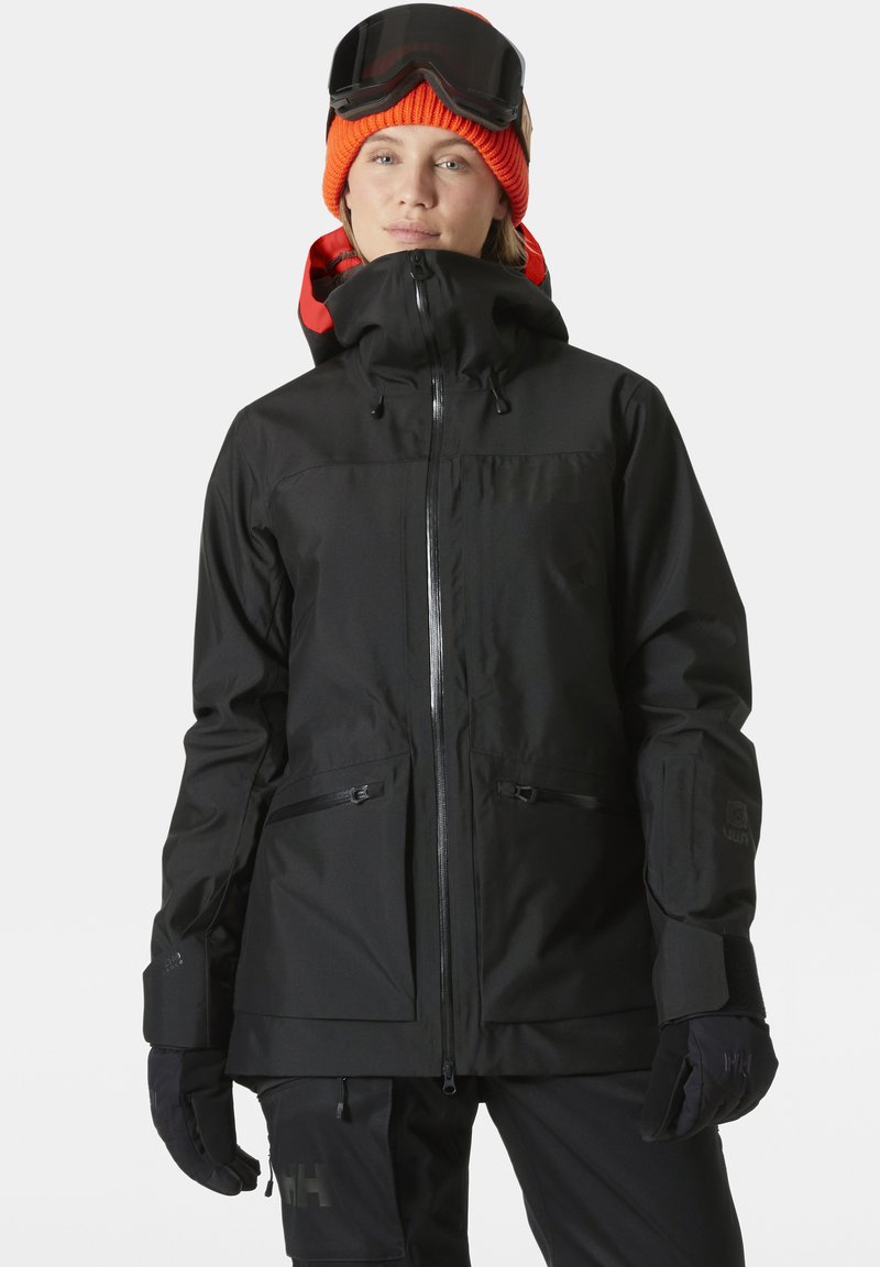 Černá zateplená lyžařská bunda s vysokým límcem, zapínáním na zip a kapsami. Má voděodolný materiál a nastavitelnou kapuci. Společně s rukavicemi.