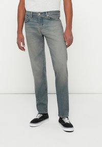 Blugi din denim de culoare albastru deschis, cu croială dreaptă, ușor decolorat în față. Prezintă un sistem de închidere cu nasture și un design clasic cu cinci buzunare.