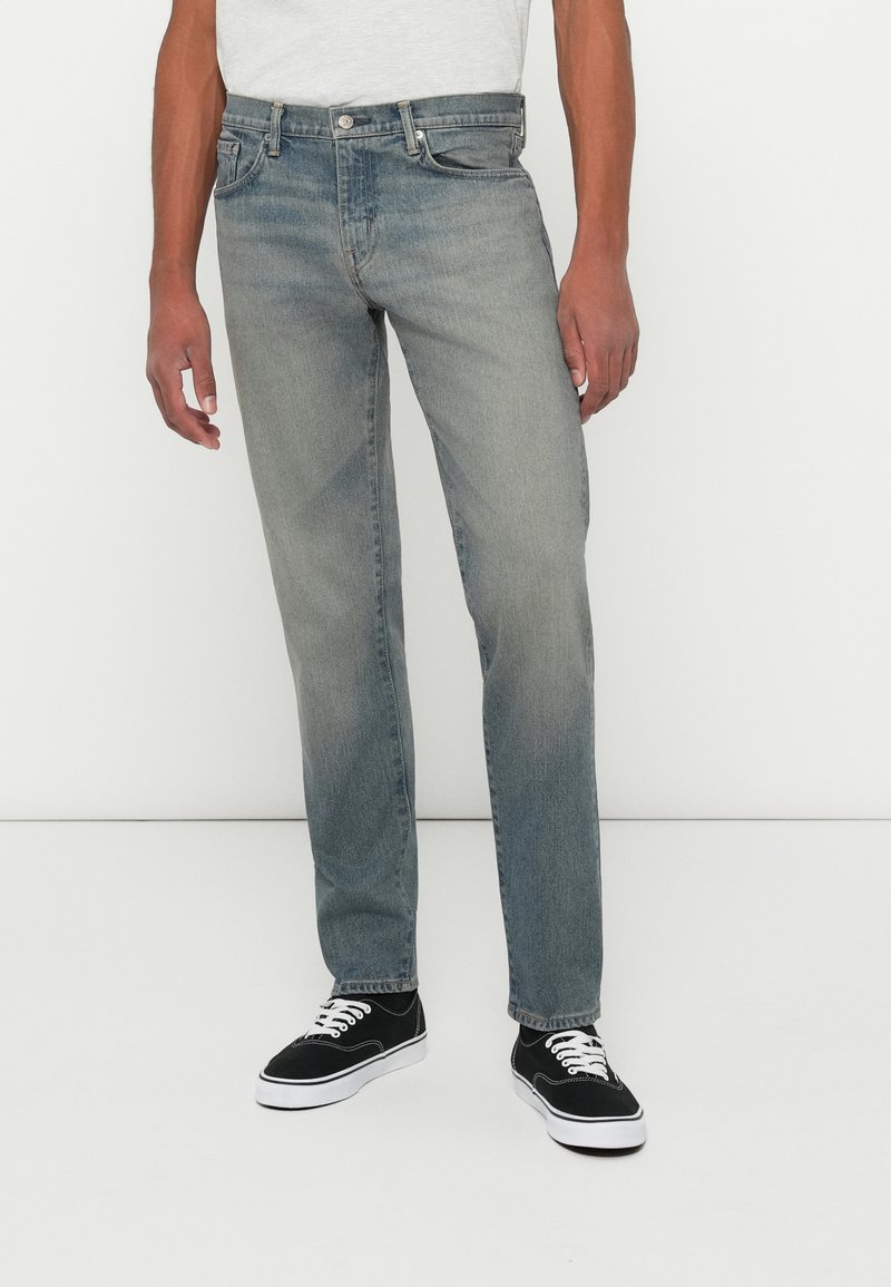 Blugi din denim de culoare albastru deschis, cu croială dreaptă, ușor decolorat în față. Prezintă un sistem de închidere cu nasture și un design clasic cu cinci buzunare.