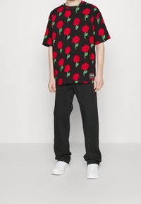 Svart t-shirt med ett mönster av ljusröda rosor, kortärmad och rund hals. Matchas med svarta byxor och vita sneakers. Anmärkningsvärd tygtextur.