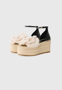 Sandalias de cuña de esparto de cuero negro con un volante de tela beige, plataforma de yute trenzado y correa al tobillo con hebilla dorada.