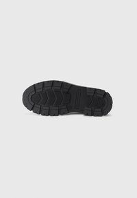 Black rubber shoe sole with deep treads, textured surface, and removable insole. Features brand logo and visible construction details.