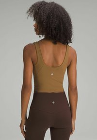 Pruunist sobivast tank topist, millel on ümmargune tagumine osa, koos kõrge vöökohtadega tumepruunide retuusidega. Materjal näib olevat veniv ja sujuv; retuusidel on logo detail.