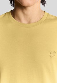 Gul bomulds T-shirt med rund hals og korte ærmer, med et lille broderet logo på venstre brystområde.