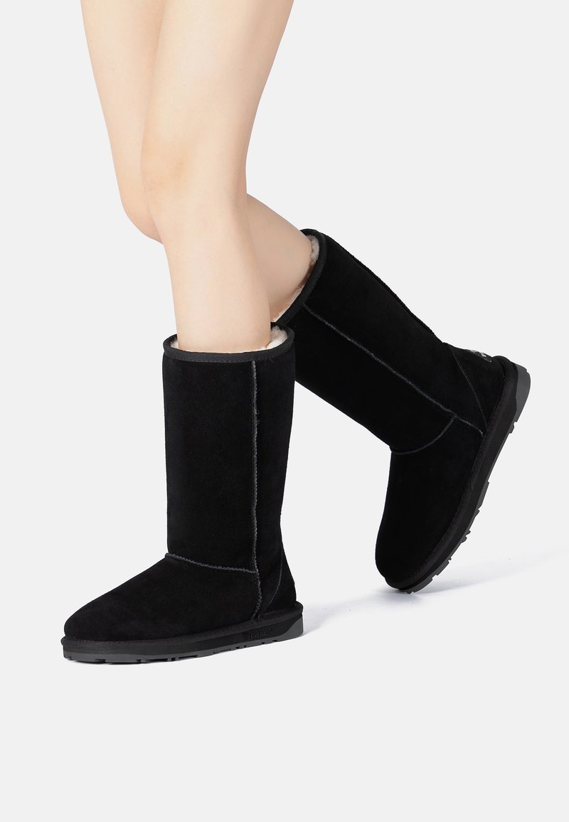 Black suede knee-high boots with a soft inner lining, flat rubber sole, and contrasting stitching. Smooth texture with a sleek design.