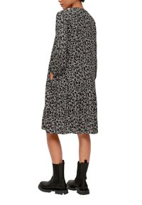 Schwarzes Blumenkleid mit langen Ärmeln und einem knielangen Rock, mit lockerer Passform und seitlichen Taschen. Kombiniert mit schwarzen Knöchelstiefeln.