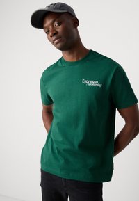 Green cotton t-shirt with short sleeves, crew neckline, and white "Espresso Awakening" text on the left chest. Smooth texture.
