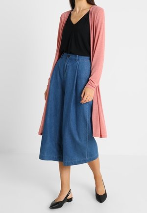 Lehký růžový cardigan s dlouhým rukávem přes černý top, ve spojení s modrými džínovými culottes s širokými nohavicemi a černými balerínami s přezkami.