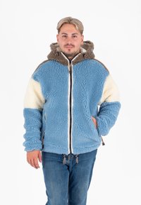 Fleecejack van blauwe stof met een crème accent en een bruine capuchon. Het heeft een ritssluiting aan de voorkant, een gestructureerde stof en verstelbare trekkoorden aan de onderkant.