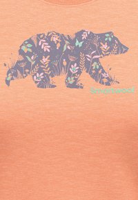 Ljusorange t-shirt med en bj�örnsilhuett fylld med blommönster i lila, rosa och grönt. Märkesnamnet "Smartwool" i teal.