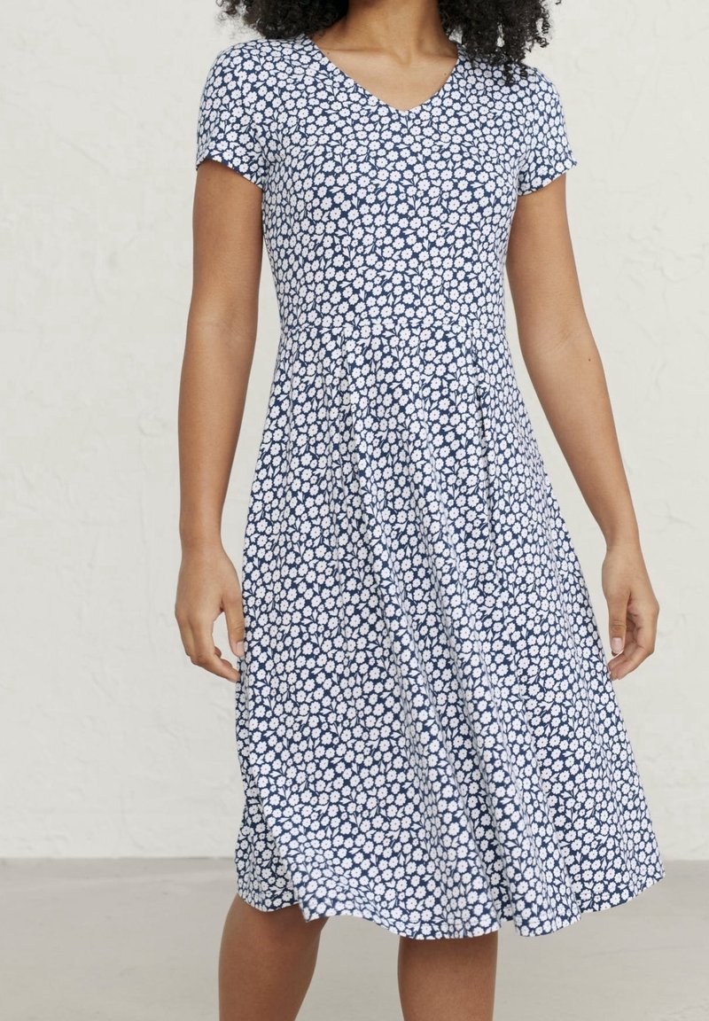 Modro-bílá květinová šaty s výstřihem do V, krátkými rukávy a rozšířenou sukní. Vyrobené z měkké tkaniny, s malým vzorem sedmikrásek.
