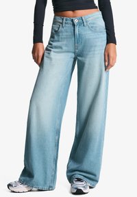 Široké světlé modré denimové džíny s mírným praním, vysokým pasem, velkými kapsami a jemným vyblednutím. V kombinaci se stříbrnými teniskami.