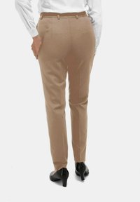 Beige op maat gemaakte broeken met een gladde textuur, achterste plooien en een subtiele glans, gedragen met zwarte hakken.