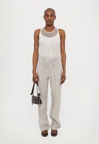Zilveren mesh tanktop met een aansluitende structuur, gecombineerd met lichtgrijze geplooide broek, met een kleine bordeauxkleurige handtas met zilveren hardware.